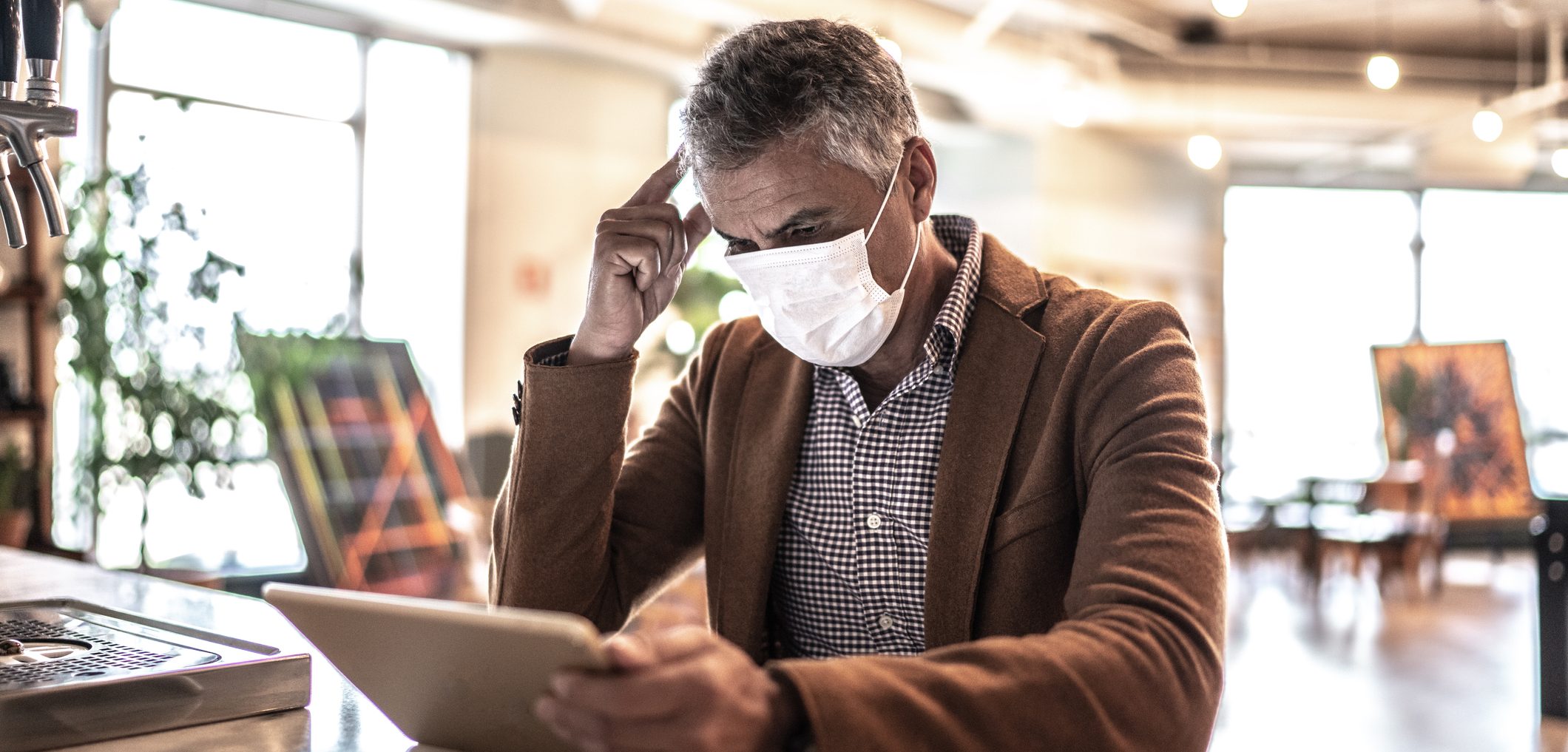 Mature businessman with mask using digital tablet at work